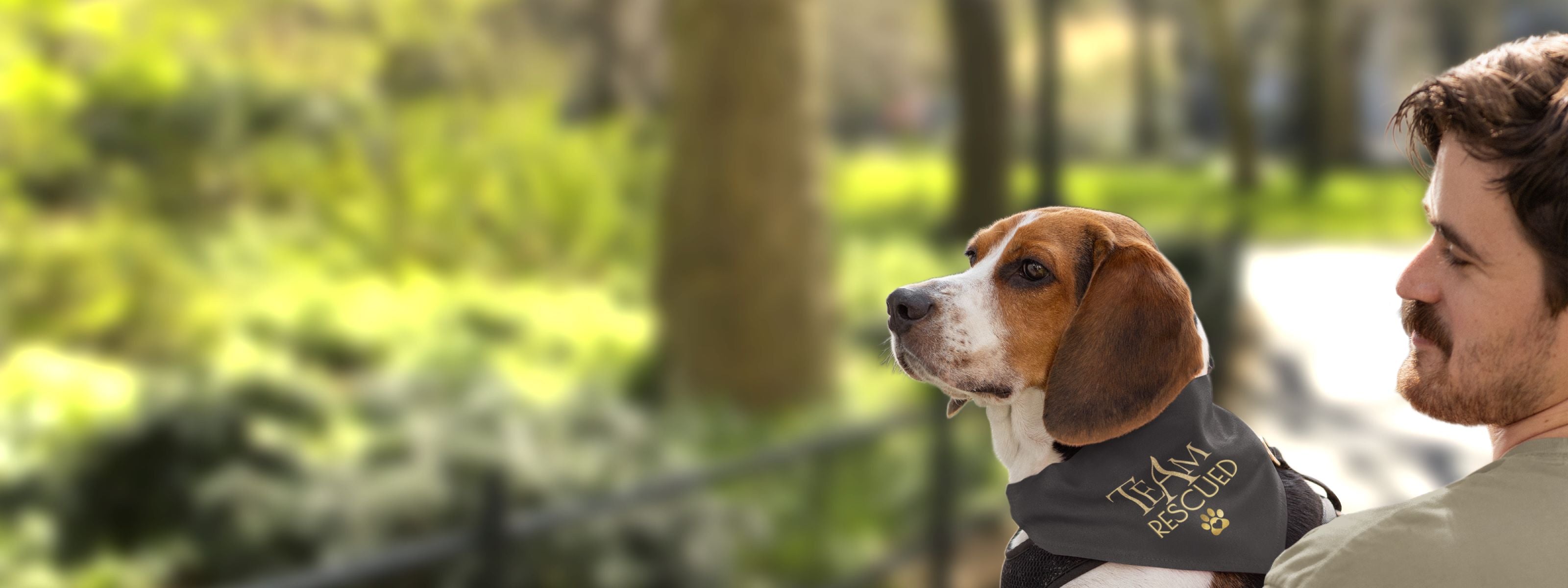 Man carrying dog wearing bandana saying Team Rescued to promote pet adoption awareness.